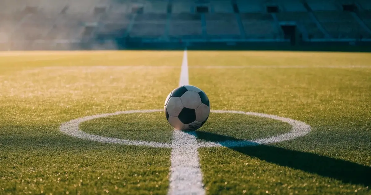 Uma bola de futebol no ponto central de um relvado, à luz da manhã